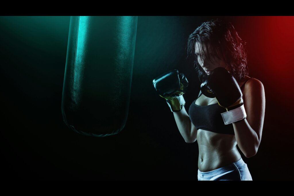 Powerful image of a woman boxer preparing to train with a punching bag in a dramatic dark setting.