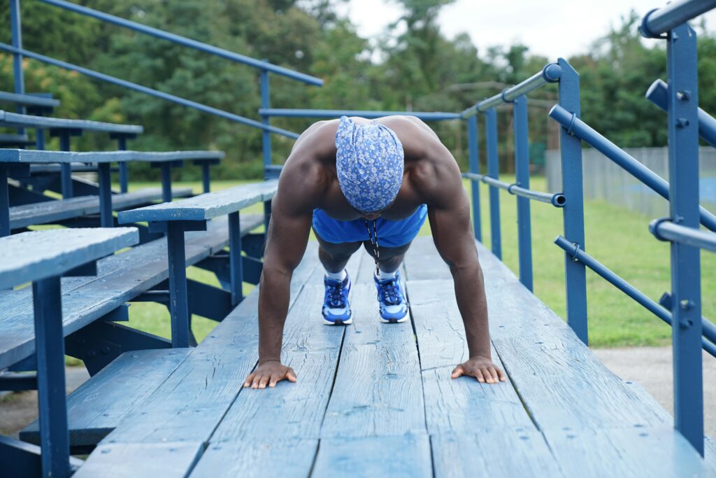 Black man performing push-ups on blue sports bleachers outdoors, enhancing strength and endurance.