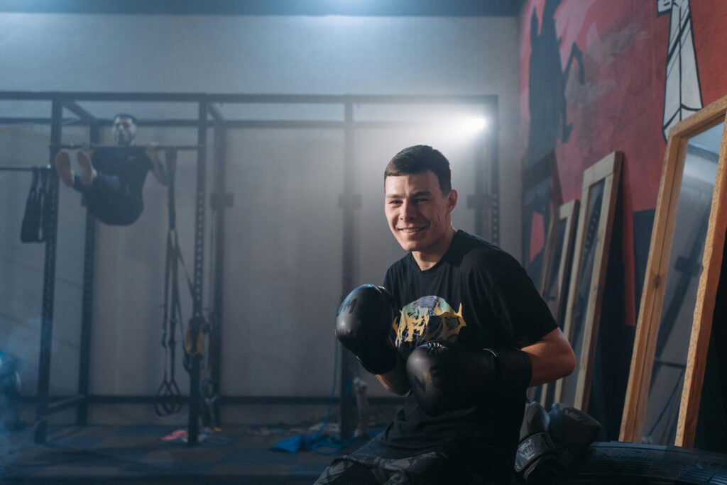 Smiling man with boxing gloves sitting in a gym, ready to fight.